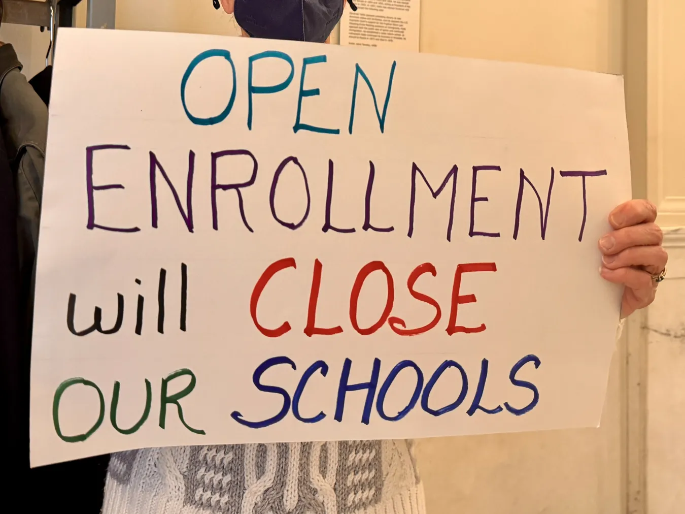 A sign reads "Open Enrollment will Close Our Schools"
