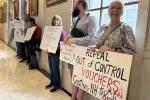 NEA-NH Board Member Tracy Bricchi holds a sign in the State House hallway.