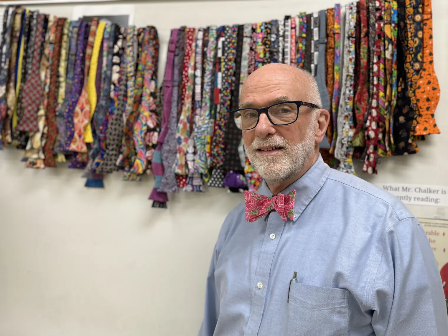 Skip Chalker stands in front of an array of his handmade bow ties, strung up in front of a white board.