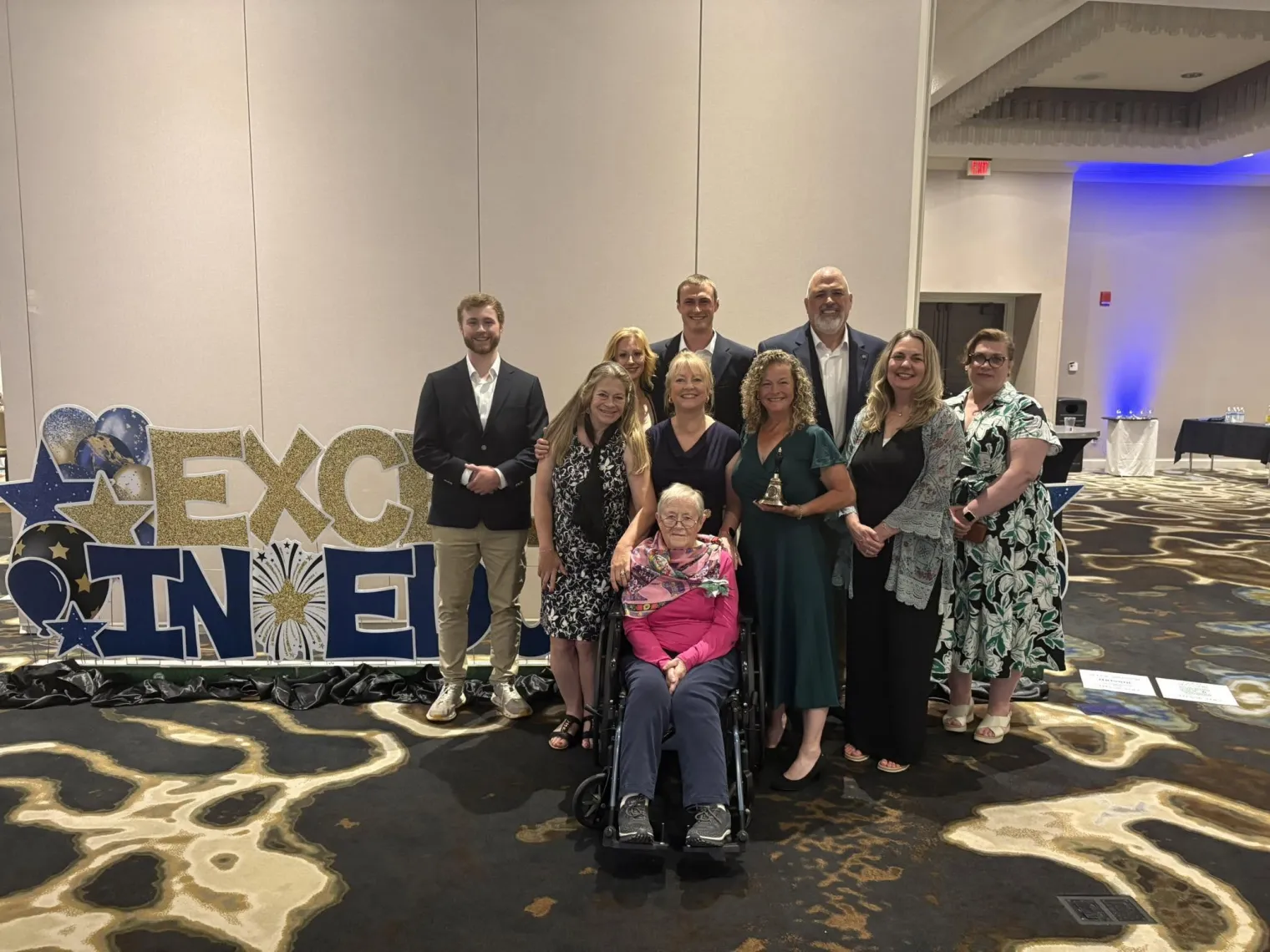 Sue Eno stands before an Excellence in Education banner with her supporters after receiving the 2026 NH ESP of the Year Award