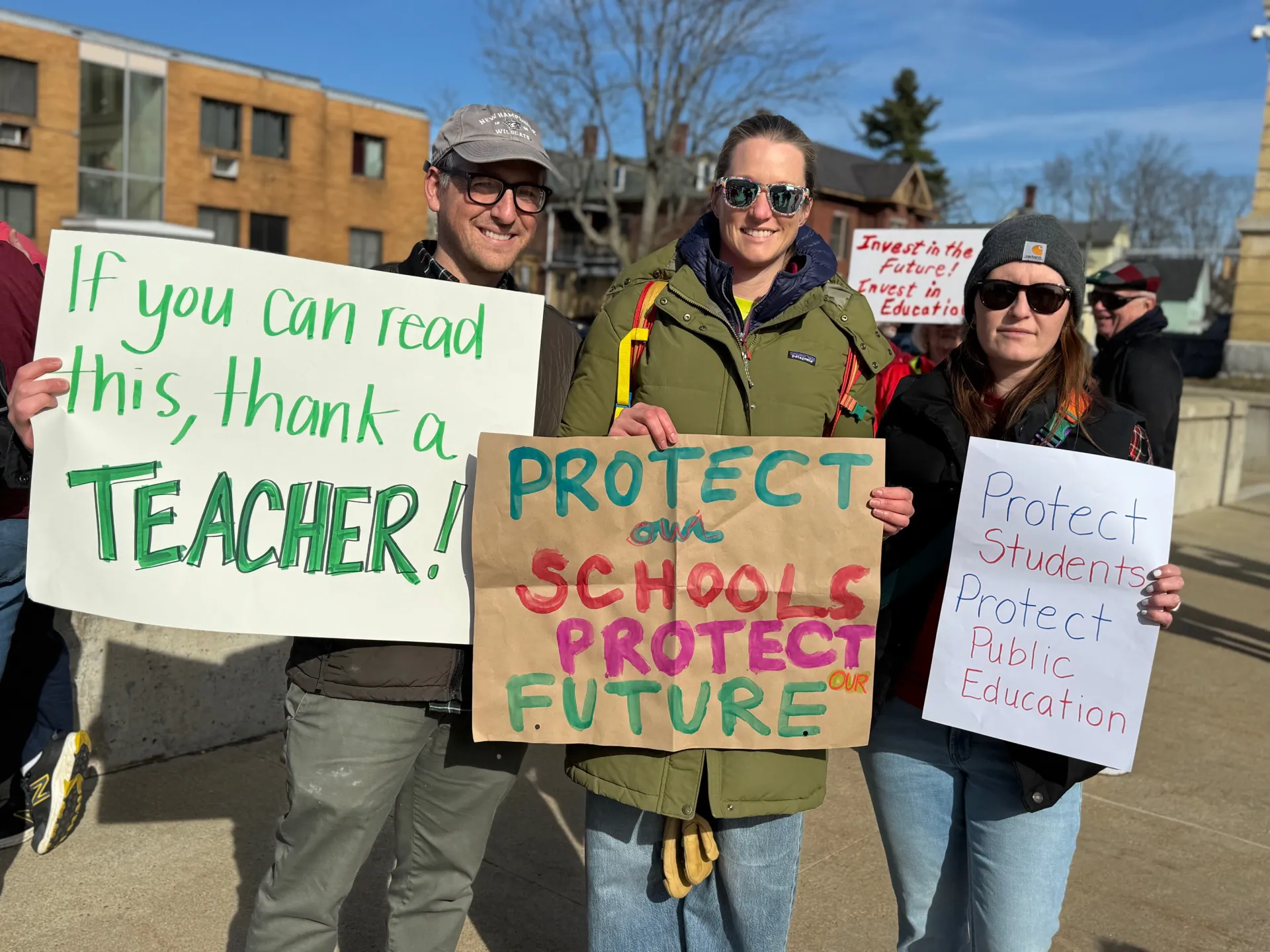 An image of three individuals holding signs supporting public education.