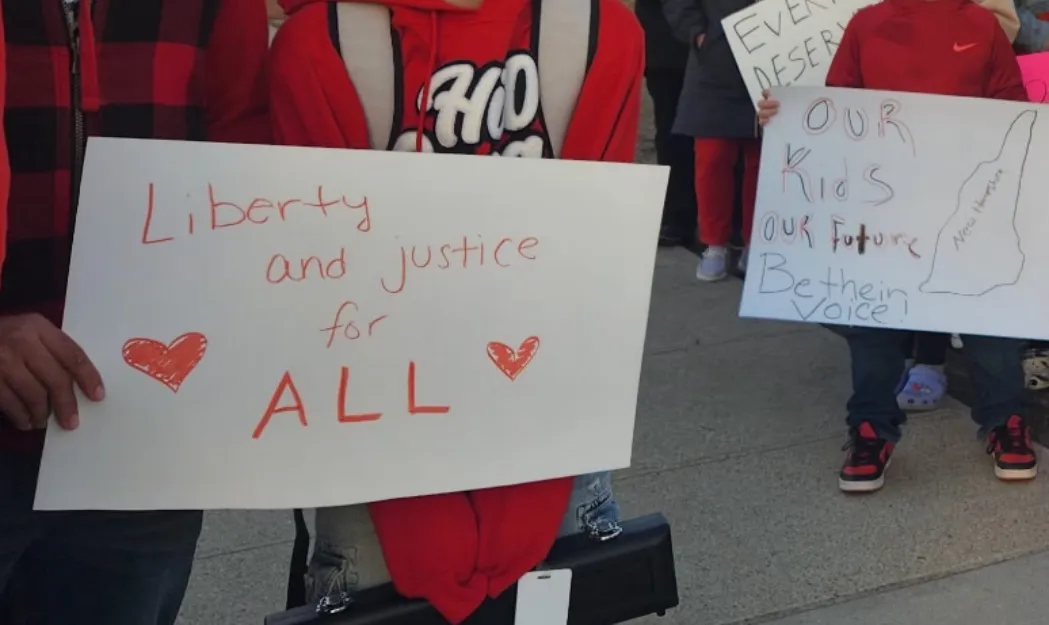 An image of someone holding a sign that reads "Liberty and Justice for All"