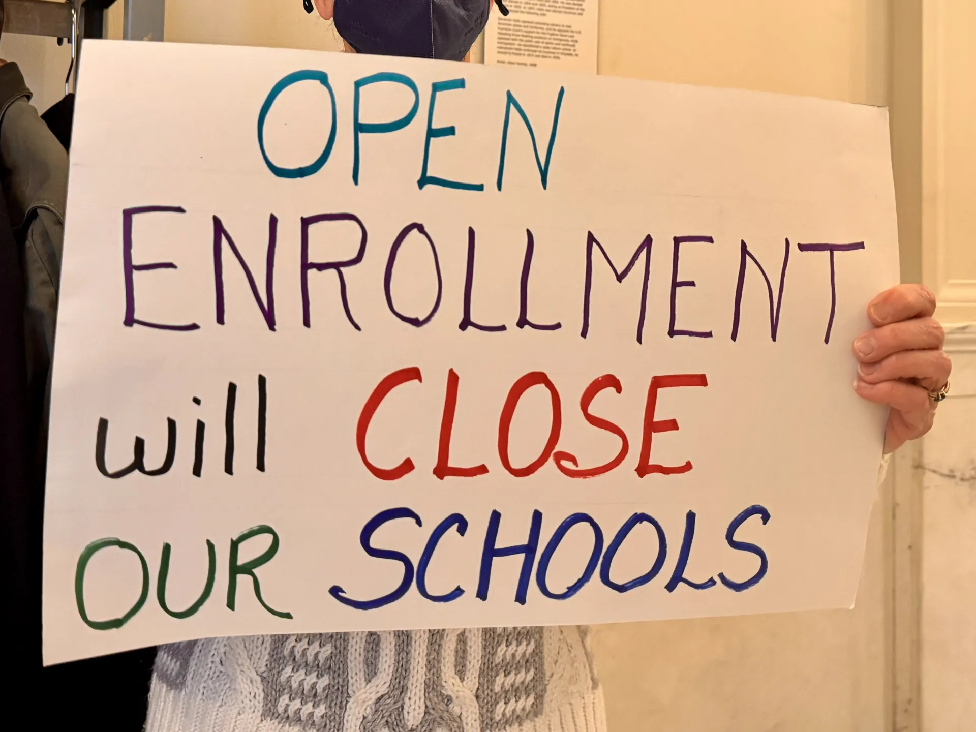 A sign reads "Open Enrollment will Close Our Schools"