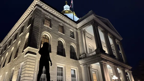 An image of the New Hampshire State House at night, with the Christa McAuliffe statue in the foreground.