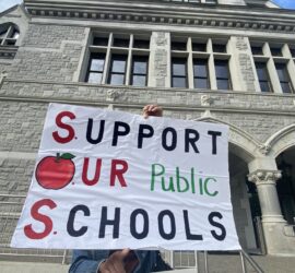 A white sign held in front of the Legislative Office Building reads: Support Our Public Schools"