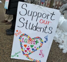A sign reads "Support our Students" with a rainbow heart that says "LGBTQ" in the center.